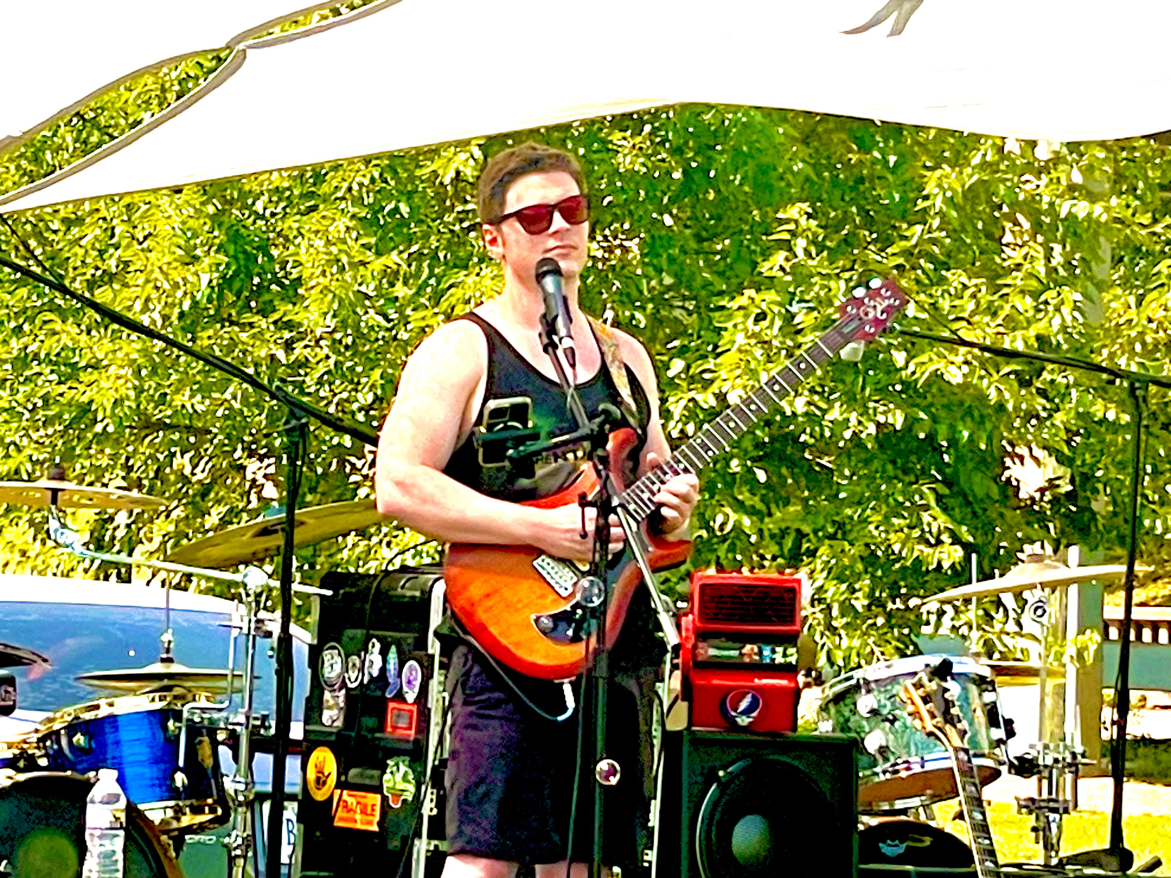 Julian Goddard singing and playing his orange electric guitar at an outdoor show
