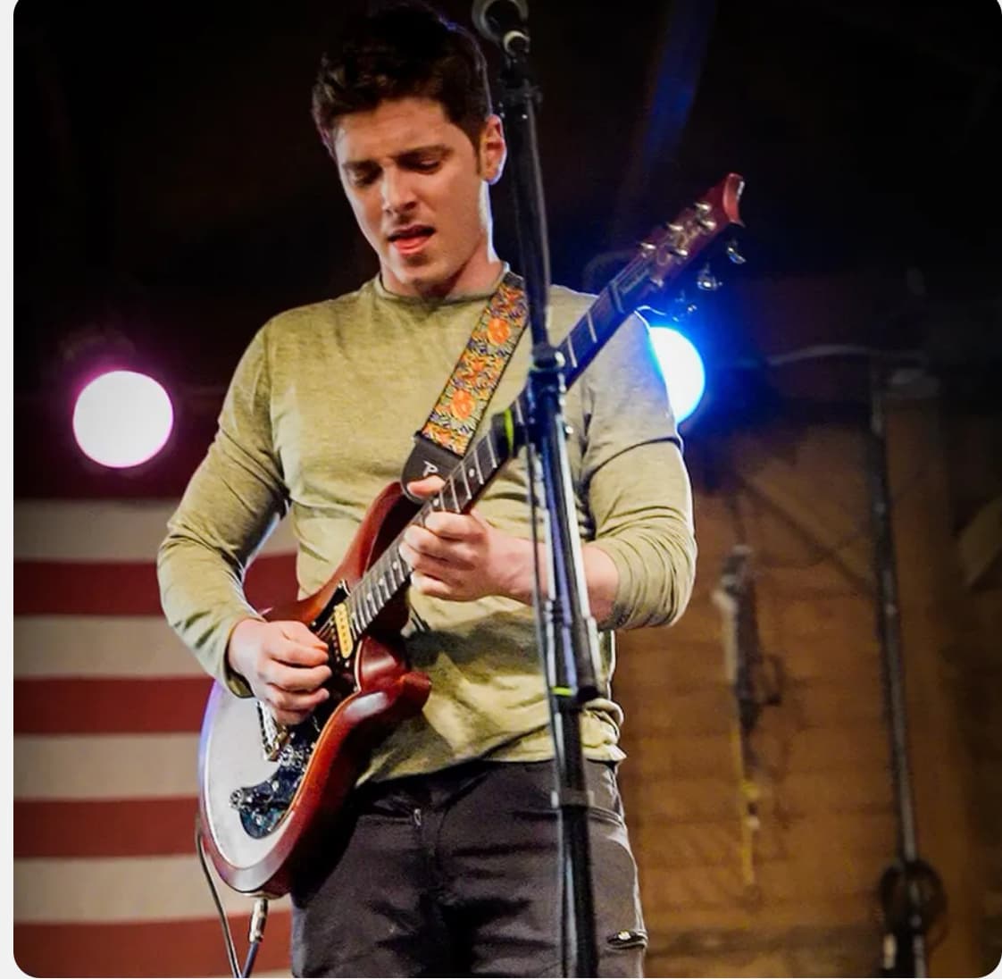Julian Goddard playing his guitar on stage under pink and blue lights